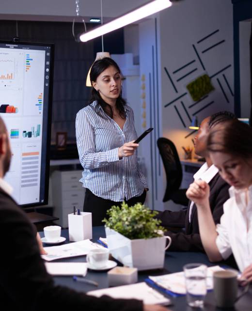 Overworked focused diverse businesspeople working in business company meeting office room brainstorming marketing strategy late at night. Entrepreneur woman presenting financial ideas